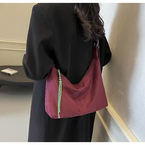 Détail d'un sac hobo en daim bordeaux avec cordon tressé vert porté par un mannequin