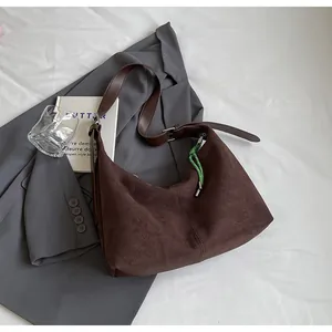 Détail d'un sac demi-lune en daim marron avec boucle argentée et accessoire tressé