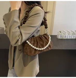 Detail of a brown ruched cloud bag featuring a glossy texture and large pearl handle strap