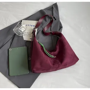 Détail du sac hobo en daim bordeaux avec bandoulière réglable et nœud tissé vert vif