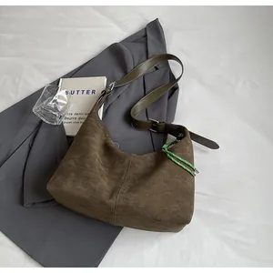 Détail du cabas en daim marron avec sa bandoulière réglable en cuir vert et son ornement