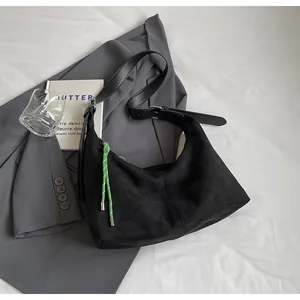 Détail d'un sac hobo en daim noir avec une cordelette verte tressée et boucle métallique