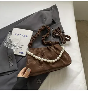 Detail of dark brown pleated handbag with pearl handle and leather straps on grey suit jacket