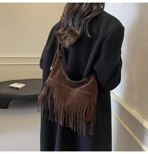 Detail van een donkerbruine suède crossbodytas met lange franjes op de schouder gedragen