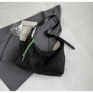 Détail du sac hobo en daim noir avec pendentif vert tressé sur un blazer gris chic