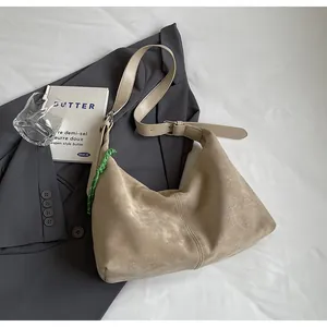 Détail du sac hobo en daim beige avec breloque en corde verte sur blazer gris
