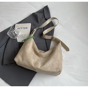 Détail du sac hobo en daim beige avec sangle réglable et breloque tissée verte sur lit