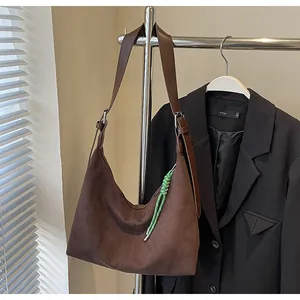 Gros plan d'un sac cabas en daim marron avec pendentif tressé vert sur cintre