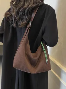 Sac fourre-tout marron en daim avec breloque verte porté par un mannequin femme