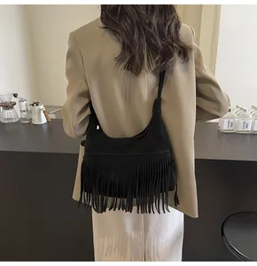 Detailweergave van de zwarte suède crossbodytas met lange franjes getoond op een persoon