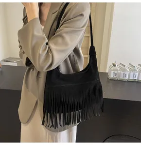 Detail van zwarte suède hobo tas met franjes gedragen op een camelkleurige blazer
