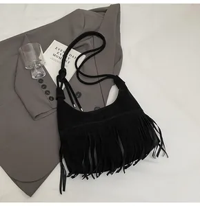Detail van zwarte suède tas met franjes en geknoopte schouderband op grijze blazer