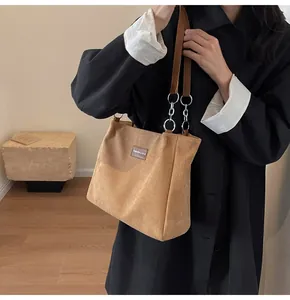 Detalle del bolso de pana marrón con etiqueta de cuero y correa de cadena metálica