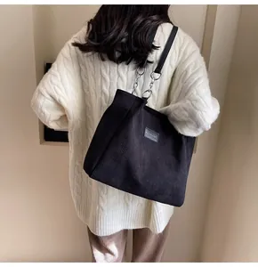 Detalle de bolso tote de pana negra con correa de cadena metálica y parche de moda