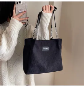 Detalle del bolso tote de pana negra con parche de logo de cuero y correa de cadena plata