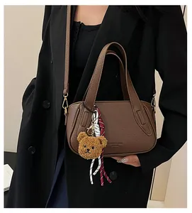 Detail of dark brown lychee leather handbag with plush bear charm and woven cord decor