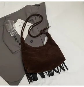 Detailopname van donkerbruine suède hobo tas met zwarte franjes en geknoopte schouderriem