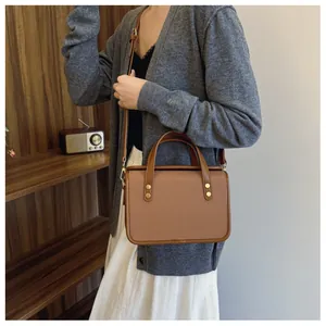 Détail du sac à main en toile marron avec bordure en cuir et rivets dorés sur fond en bois