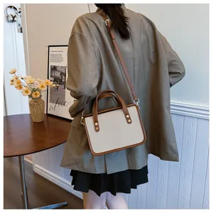 Détail du sac bandoulière en toile et cuir marron porté par un mannequin dans un intérieur