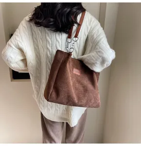 Detalle del bolso tote de pana marrón oscuro con cadena y etiqueta de cuero en el hombro