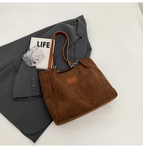Detalle del bolso tote de pana marrón café con textura vertical y parche de cuero con logo