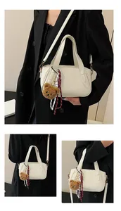 Detail of cream lychee texture leather bag with cute bear charm and woven ribbon strap