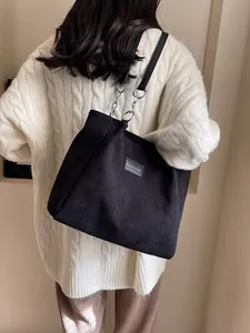 Bolso tote de pana negra con correa de cadena mostrado en vista trasera de modelo