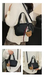 Detail of black litchi texture leather handbag with gold hardware and plush bear charm