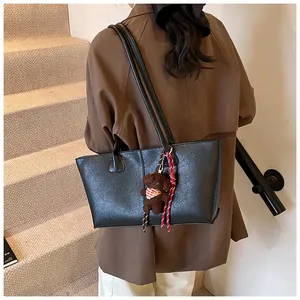 Detail van zwarte lederen tote bag met een schattige pluche beer hanger en lange riemen