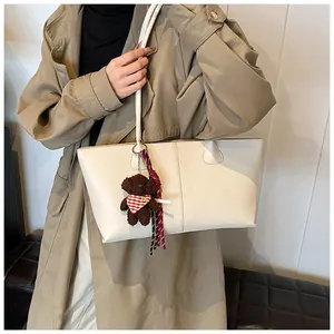 Detail van een crèmekleurige shopper met verticale stiksels en beertje hanger