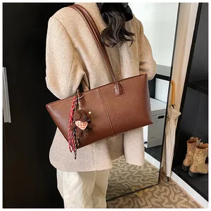 Detail van donkerbruine leren tote bag met een schattige teddybeer hanger en riemen