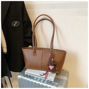 Detail van bruine shopper tas op koffer met pluche beer hanger en decoratief lint detail