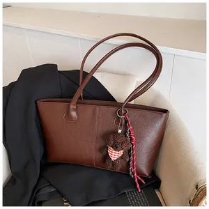 Detail van donkerbruine leren tote bag met een teddybeer hanger op een colbertjas