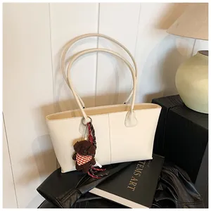 Detail van minimalistische beige draagtas met lange hengsels en een schattige beer hanger