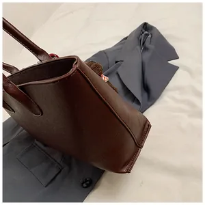 Detail van de bruine tote bag van getextureerd leer met een rode pluchen hanger