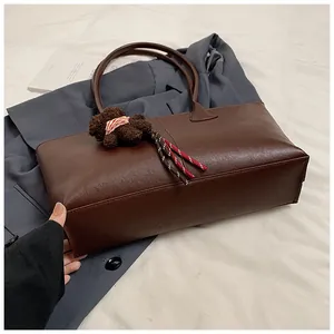 Detail van donkerbruine leren tote bag met een schattige berenhanger op witte stof