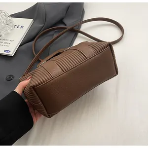 Détail de la texture cuir litchi et du design plissé sur un sac bandoulière marron