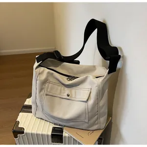 Detail of a beige canvas messenger bag with black strap resting on a white suitcase