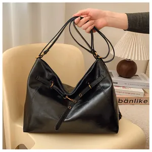 Detalle del bolso tote de cuero negro con herrajes dorados y correas decorativas