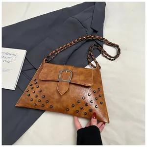 Detail einer braunen PU-Leder Umhängetasche mit Nieten und Kettenriemen auf einem Blazer