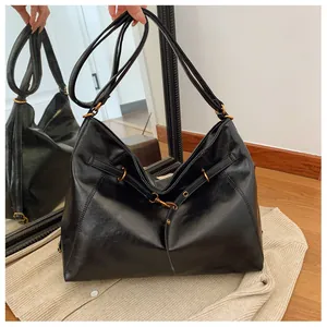 Vista detallada de la textura de cuero negro brillante y la hebilla dorada del bolso tote