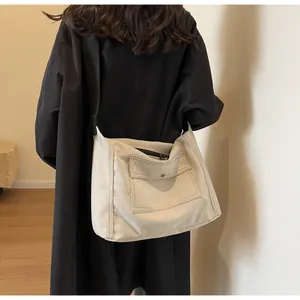 Detail view of large cream canvas messenger bag worn crossbody over a black coat