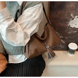 Detail of dark brown pleated tote bag featuring tassel charm and textured vertical folds