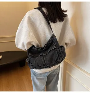 Close-up of oversized dark grey washed denim messenger bag with multi-pocket workwear design