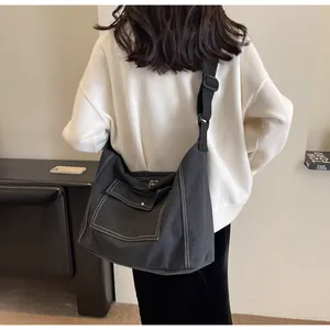 Detail of black canvas messenger bag featuring white contrast stitching and a front flap pocket