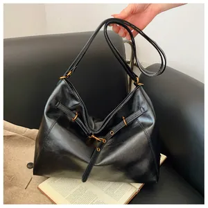 Detalle de bolso de hombro en cuero sintético negro con herrajes dorados y correa