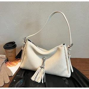 Close-up of cream corduroy tote bag featuring decorative tassels and smooth leather straps