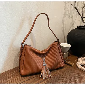 Detail of vintage brown leather tote with pleated texture and tassel pendant on wood table