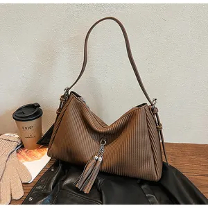Detail of dark brown pleated tote bag with tassels and metallic chain on a wooden table