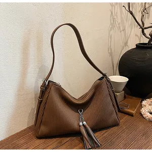 Detail of a brown pleated tote bag featuring a silver chain tassel on a wood table